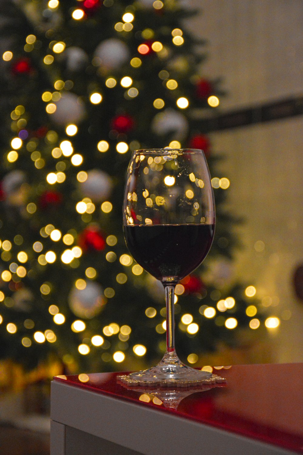 a glass of wine sitting on a table in front of a christmas tree