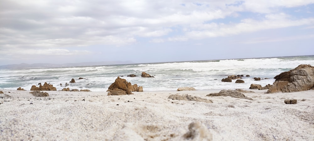 ein Sandstrand mit Felsen und Wasser im Hintergrund