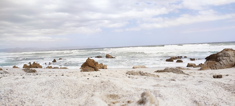 a sandy beach with rocks and water in the background