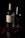 A glass wine bottle labeled 'Calabria Family Wines Bèlena True Partnership Rosé 2021' is placed alongside an empty wine glass. Surrounding the bottle are various berries, including cherries and raspberries, arranged on a reflective, dark surface which adds a dramatic ambiance to the image.