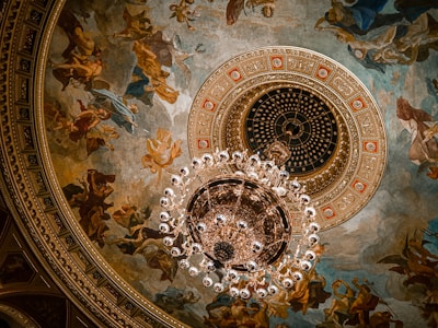 A grand chandelier casting warm light over a richly decorated European art-filled salon.