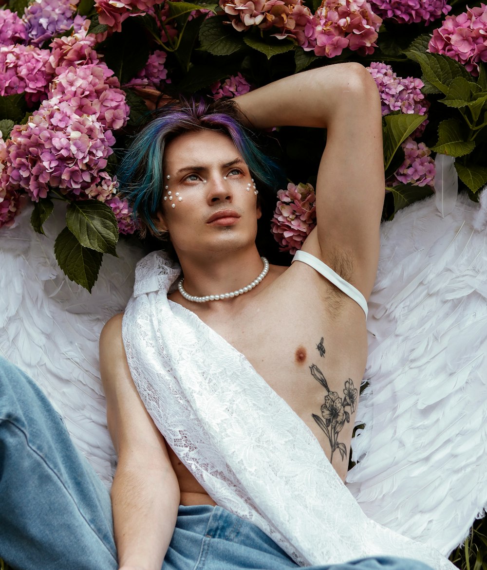 a man with blue hair laying on the ground next to flowers