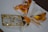 A festive, decorative item featuring a fabric napkin elaborately folded and tied with a gold and white string. It includes a tag with the words 'Merry Christmas' surrounded by gold sequins, and a golden wax seal, all placed on a white plate.