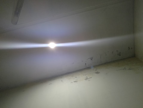 A bright light is emitting from a ceiling-mounted fixture, casting a glare across the room. The walls and ceiling appear worn and discolored, with noticeable patches and peeling paint.