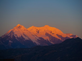 A serene sunrise over the snow-capped peaks of the Swiss Alps, with soft golden light illuminating rugged terrain.