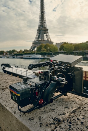 A film crew setting up cameras on a sunlit Paris street with the Eiffel Tower in the background.