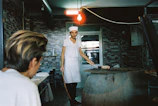 Technician carefully repairing a commercial oven in a busy restaurant kitchen.
