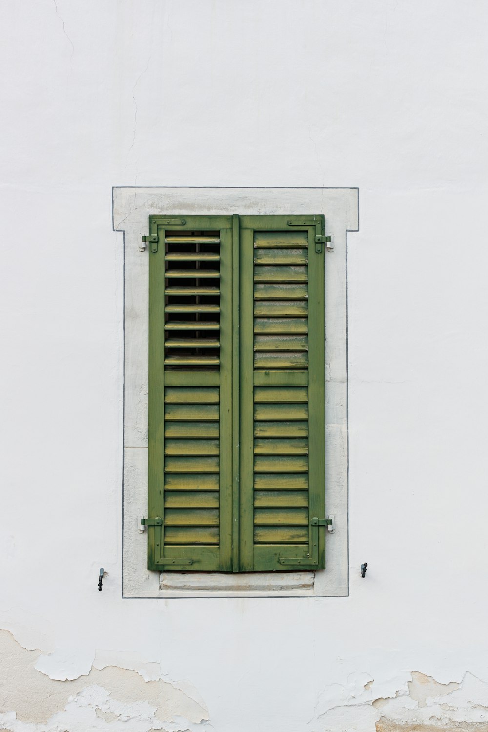 a green shuttered window on a white wall