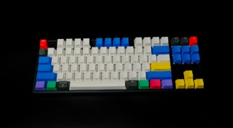 A mechanical keyboard with a variety of colorful keycaps, including white, blue, red, green, purple, and yellow. The keyboard layout features standard keys with some keys highlighted in vibrant colors, making it visually striking against a dark background.