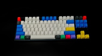 A mechanical keyboard with a variety of colorful keycaps, including white, blue, red, green, purple, and yellow. The keyboard layout features standard keys with some keys highlighted in vibrant colors, making it visually striking against a dark background.