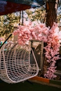 An inviting outdoor rattan swing chair hanging under a leafy tree.
