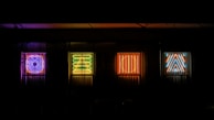 Five brightly lit neon signs against a dark background, each displaying a distinct geometric shape: a circle, a square, a triangle, and abstract designs in vibrant colors.