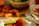 A table set up with a variety of foods, including crispy fried chicken pieces, a fresh green salad in a large bowl, and a whole ripe orange with leaves. The table is covered with a white cloth and there is a fork placed beside a ceramic plate with floral designs. The warm lighting casts soft shadows, creating a cozy and inviting atmosphere.