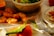A table set up with a variety of foods, including crispy fried chicken pieces, a fresh green salad in a large bowl, and a whole ripe orange with leaves. The table is covered with a white cloth and there is a fork placed beside a ceramic plate with floral designs. The warm lighting casts soft shadows, creating a cozy and inviting atmosphere.