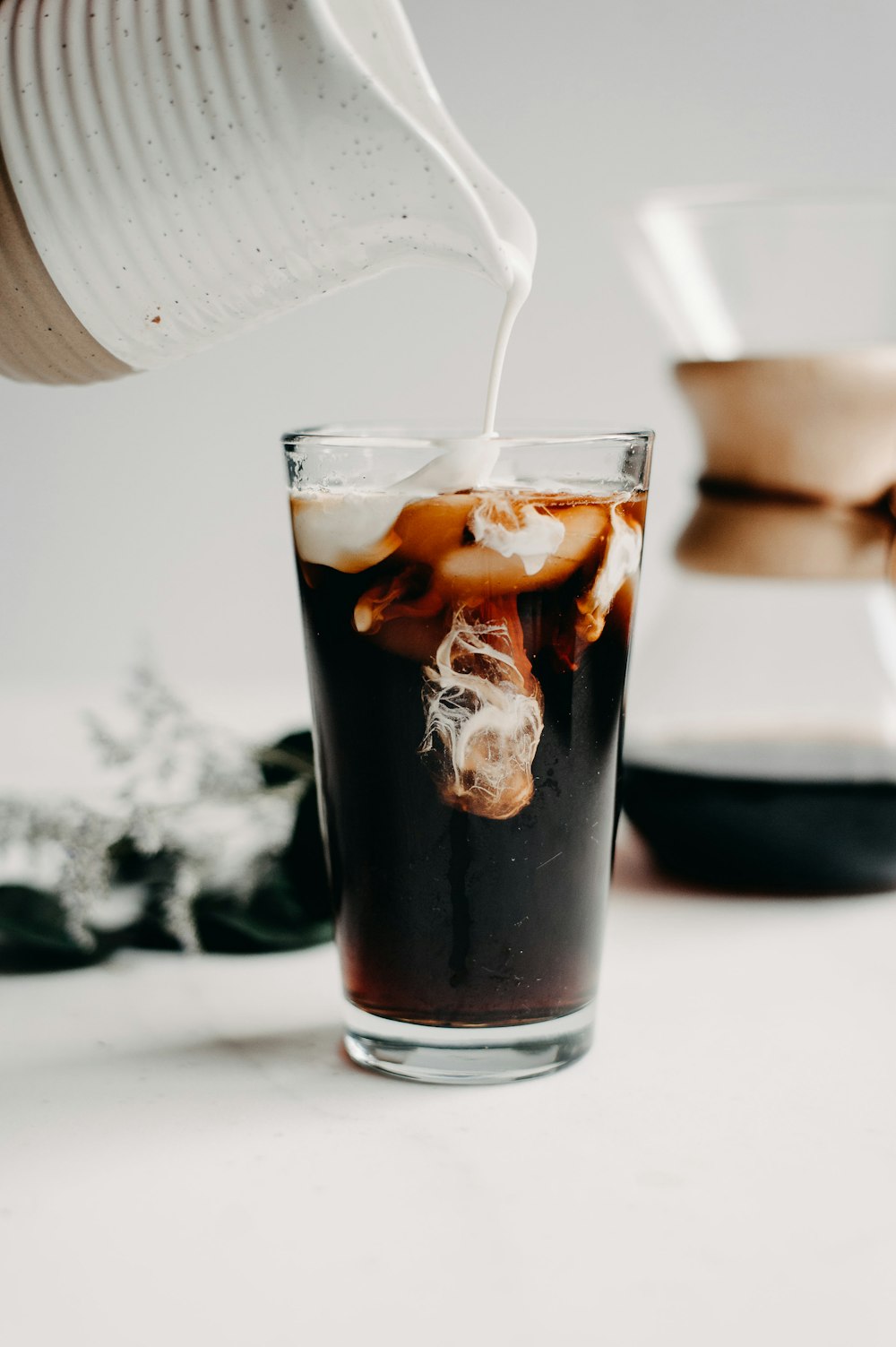 a pitcher pouring ice into a glass filled with liquid