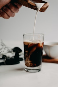 Fresh milk being poured into a glass on a rustic wooden table.