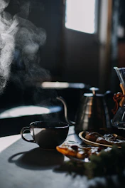 A warm, cozy coffee shop corner bathed in soft morning light with steaming cups and coffee beans scattered on a rustic wooden table.