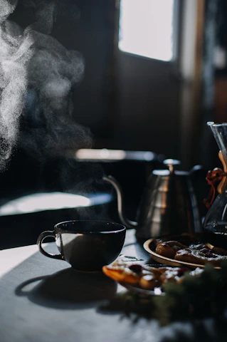 A warm, cozy coffee shop corner bathed in soft morning light with steaming cups and coffee beans scattered on a rustic wooden table.