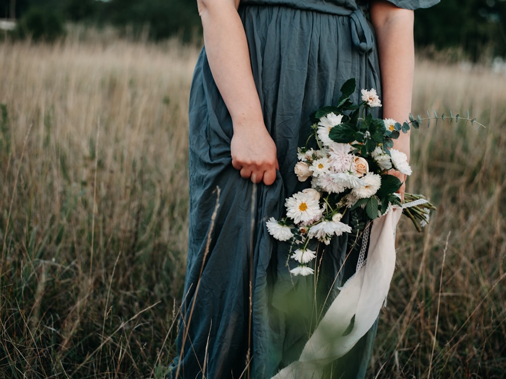 a woman standing in a field holding a bouquet of flowers