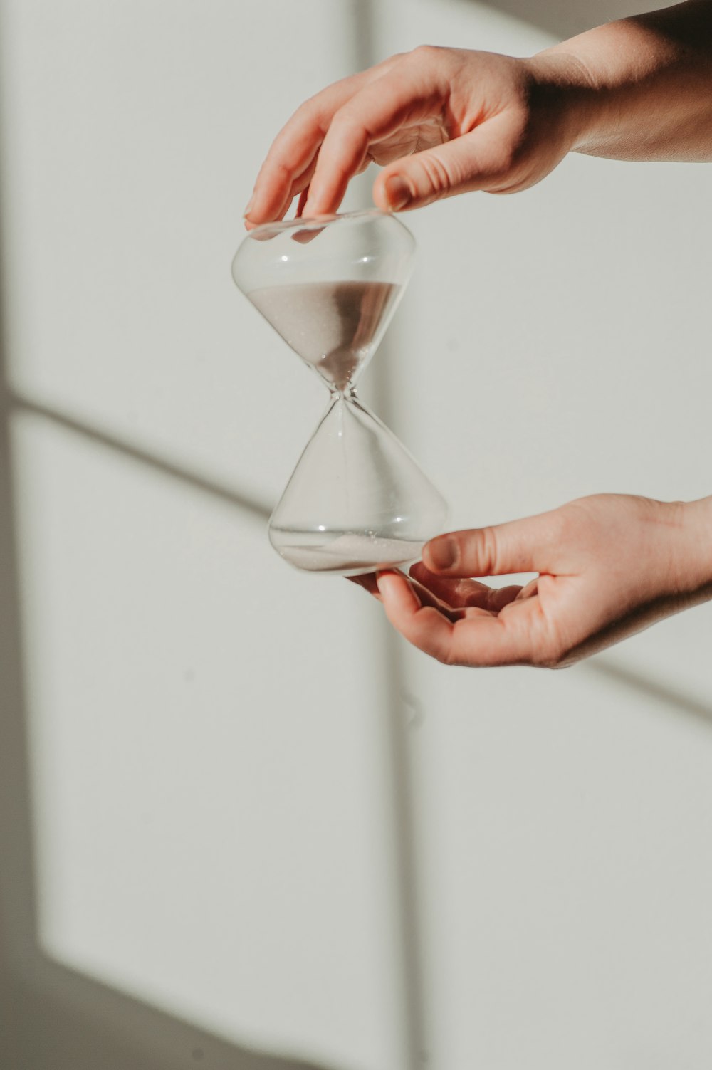 two hands holding a sand glass in front of a window