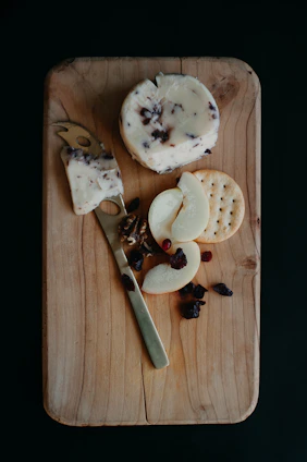 Close-up of a rustic wooden board displaying a variety of artisanal cheeses with herbs and nuts.