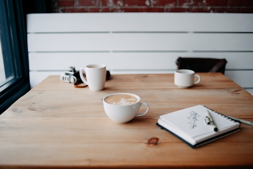 Soft-focus image of a vintage café table with a single cup of coffee and an open journal beside it.