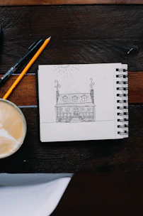 Hands sketching ideas on a notepad beside a cup of coffee on a wooden table.