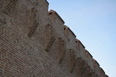 Photo of a bricklayer carefully laying bricks on a residential wall under clear skies.