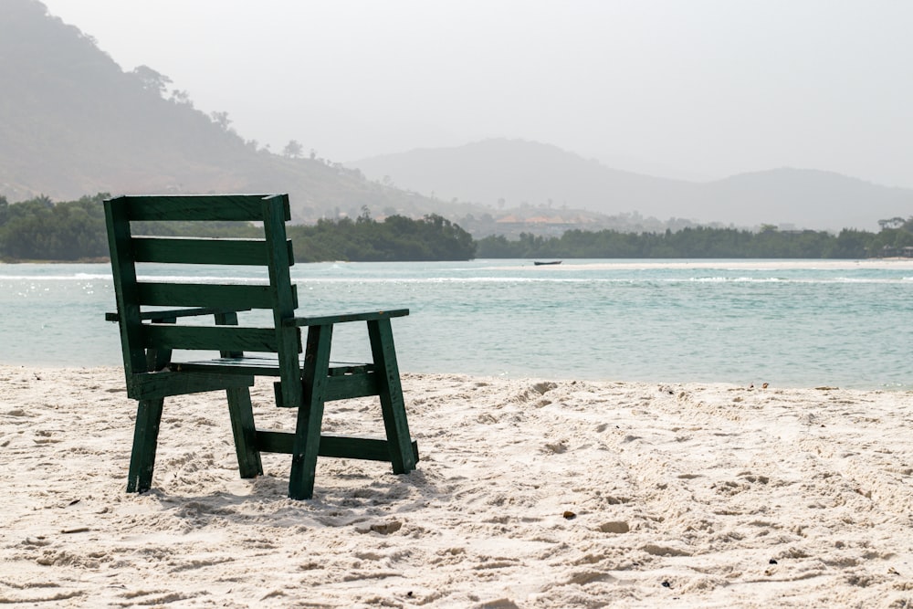 a green chair sitting on top of a sandy beach