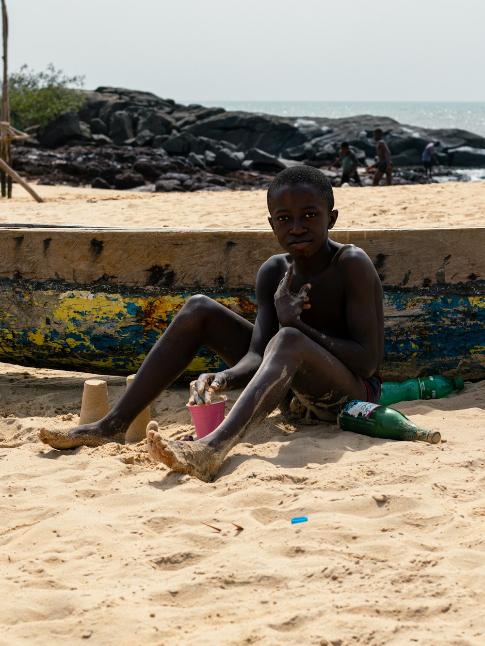 a young boy sitting on the beach next to a boat