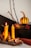Several decorative elements are arranged, including two lit yellow candles, cinnamon sticks, a dried orange slice, and a small gourd on a wooden surface. Nearby, a Harry Potter book is placed upright, alongside a branch leaning against a wall.