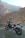 A motorcycle is parked on a rocky terrain with a backdrop of rugged mountains. The bike has a sleek design with a combination of black and gold colors, and it stands on a dirt path with an open road visible. The setting creates a sense of adventure and exploration.