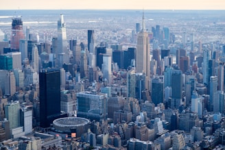 Aerial view of a sprawling metropolis featuring numerous skyscrapers and densely packed buildings. The cityscape is dominated by tall structures, including a distinctive, recognizable tower. The surrounding urban area extends into the distance, showcasing a blend of modern and older architecture.