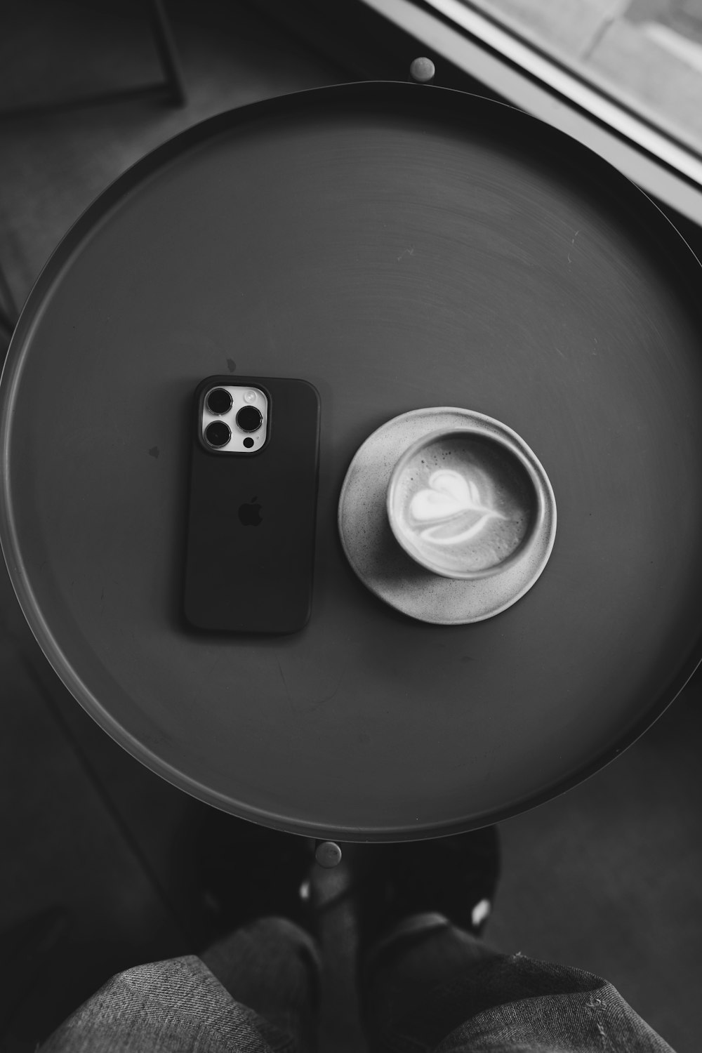 a black and white photo of a table with a cup of coffee and a cell