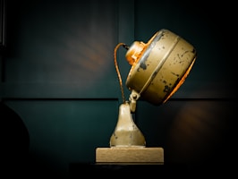 A vintage desk lamp with a brass finish casting a soft glow over a minimalist wooden sideboard.