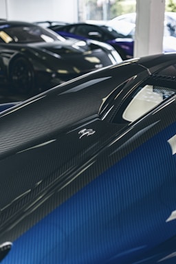 Close-up of a sleek carbon fiber car part reflecting light in a luxury garage.