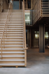 Wooden stairs with metal railings lead up to the next floor inside a modern interior space. The design features slatted wooden panels and an open area beneath the stairs, giving the structure a contemporary look.