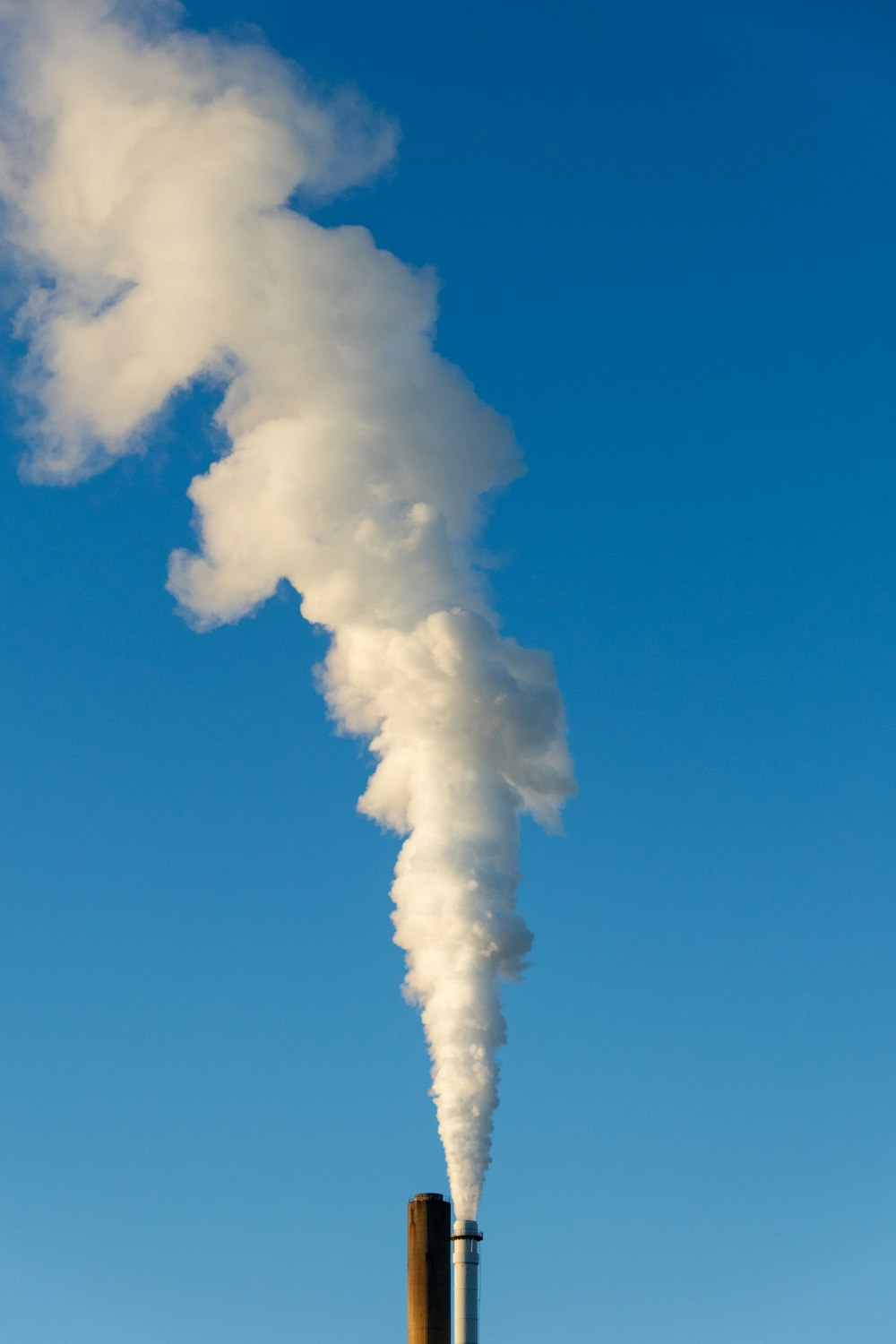 a smokestack emits from a building with a blue sky in the background