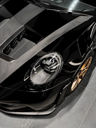 Close-up image of a sports car's gleaming black hood reflecting ambient gold lighting.
