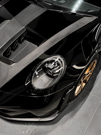Close-up image of a sports car's gleaming black hood reflecting ambient gold lighting.
