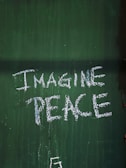 The phrase 'Imagine Peace' is written in white on a green textured surface.