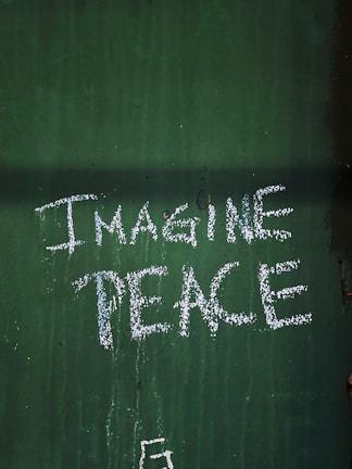 The phrase 'Imagine Peace' is written in white on a green textured surface.