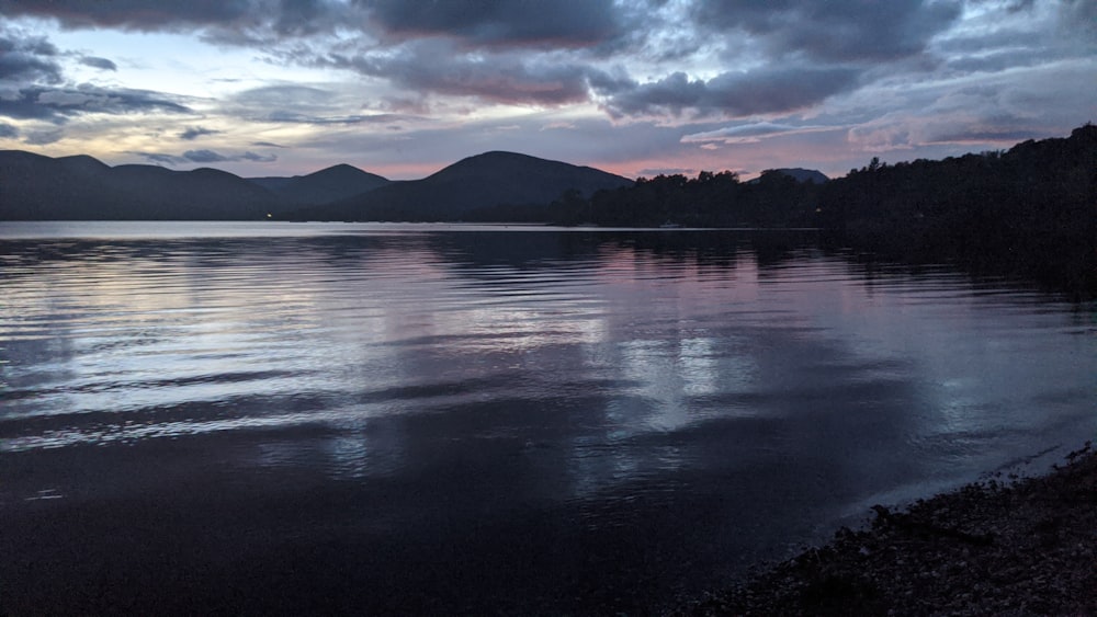 a body of water surrounded by mountains under a cloudy sky