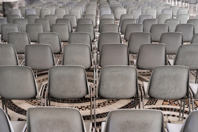 A large array of gray chairs is neatly arranged in rows, set on a patterned mosaic tile floor.
