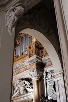 An ornate architectural interior featuring intricate sculptures and detailed carvings. The design includes angelic figures, elaborate columns, and vibrant sections of gold and blue. The overall decoration suggests a historic or religious setting.