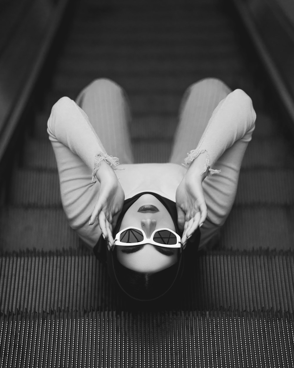 uma mulher usando óculos escuros deitada em uma escada rolante