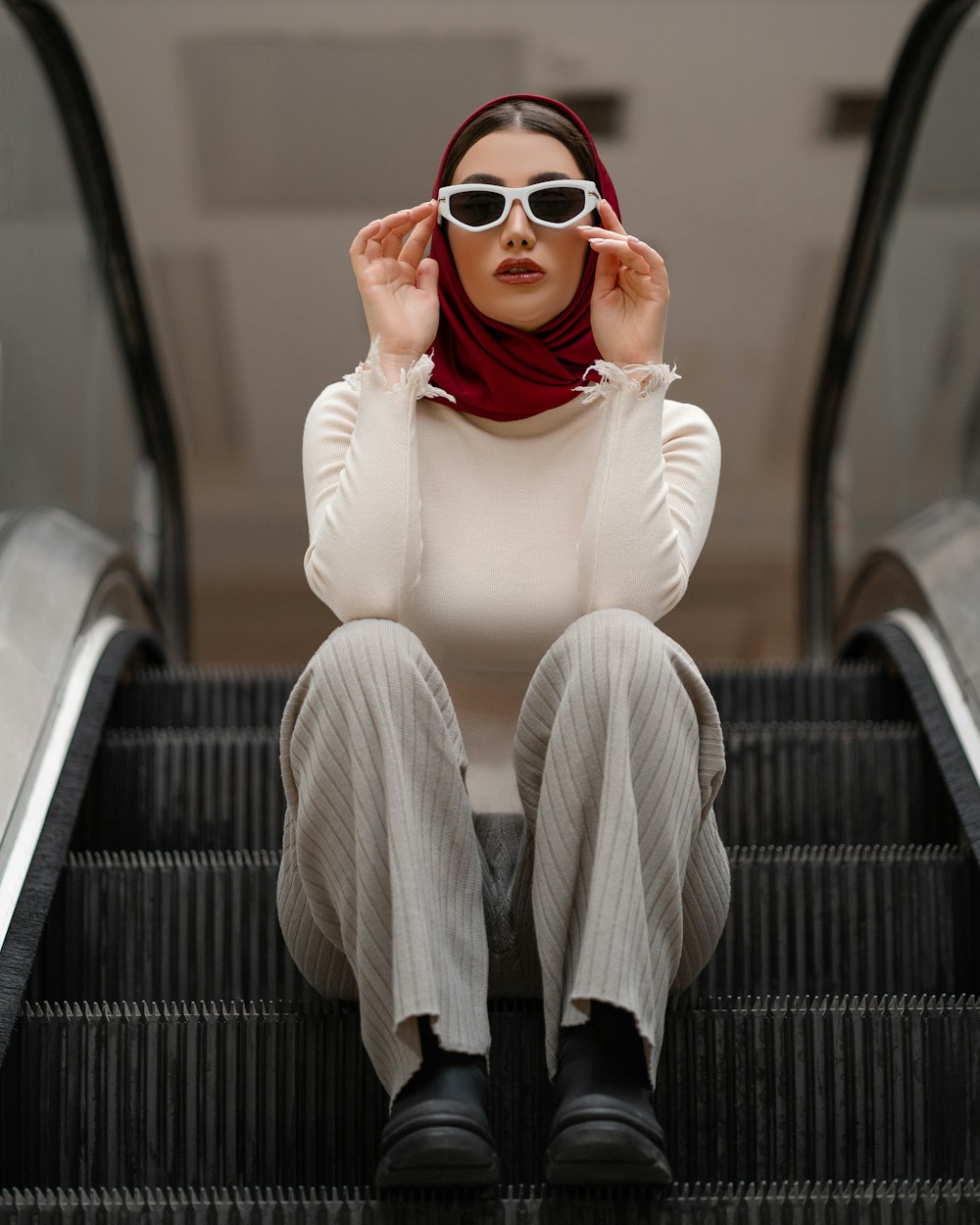 a woman sitting on an escalator wearing sunglasses and a scarf