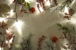 Christmas-themed decorations including sprigs of artificial pine, clusters of red berries, candy canes, baubles, and string lights are arranged around the perimeter of the image, creating a festive border on a blank background.