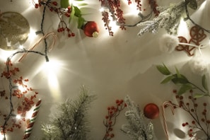 Christmas-themed decorations including sprigs of artificial pine, clusters of red berries, candy canes, baubles, and string lights are arranged around the perimeter of the image, creating a festive border on a blank background.