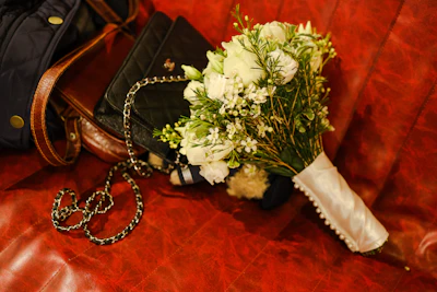 A sleek black crossbody bag resting beside a bouquet of fresh wildflowers.